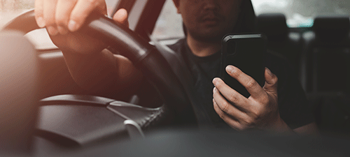 man sitting behind wheel in car, holding cell phone as if on video call