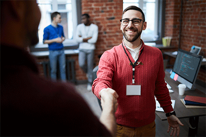 Smiling man with arm outstretched shaking hands with another person.