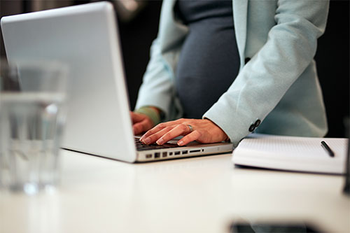 cropped image of woman standing at laptop obviously pregnant