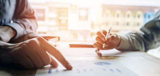 close up focusing on hands of 2 people looking over budget paperwork at desk