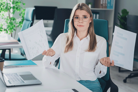 woman at desk holding paperwork in both hands looking at camera with look of confusion