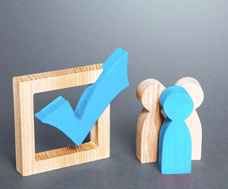 3 wooden human figures, 2 natural wood color, one blue, situated next to box with blue checkmark