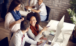 Woman at desk surrounded by employees in front of computer