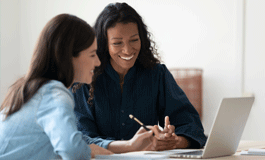 2 woman at desk looking at computer, smiling